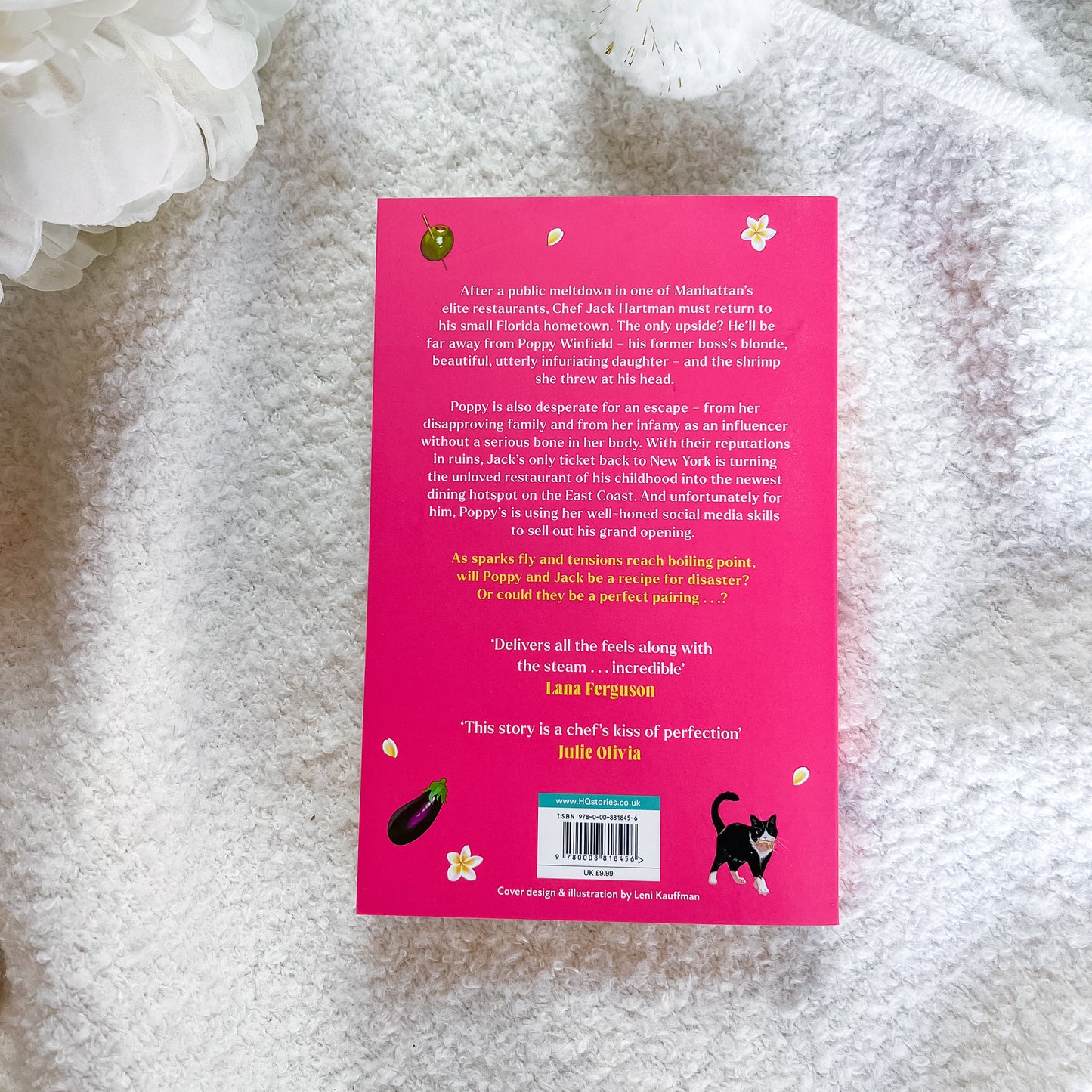 The back cover of a book, featuring a bright pink background with white and black illustrations, photographed on a textured white fabric surface.