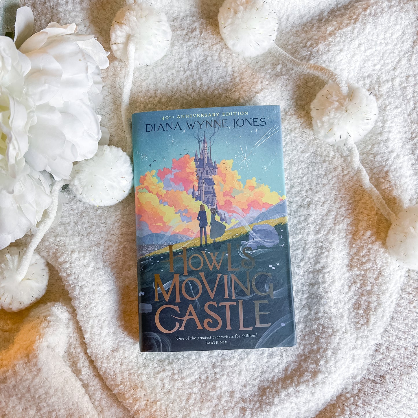 Book titled 'Howl's Moving Castle' by Diana Wynne Jones on a textured surface with white flowers.