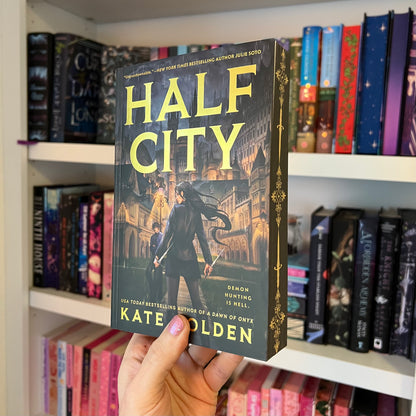 Book titled 'Half City' held in front of a bookshelf with various books.