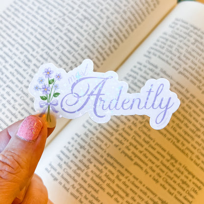 Sticker with 'Ardently' and floral design held over an open book