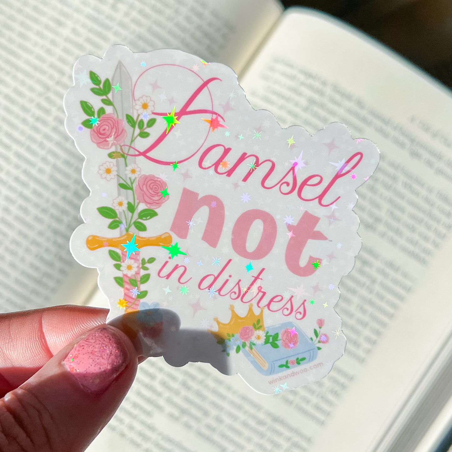 Sticker with 'Damsel not in distress' text held by a hand on a textured surface.