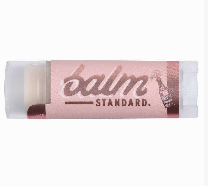 A tube of Balm Standard lip balm with a light pink label and white caps, shown against a plain white background.