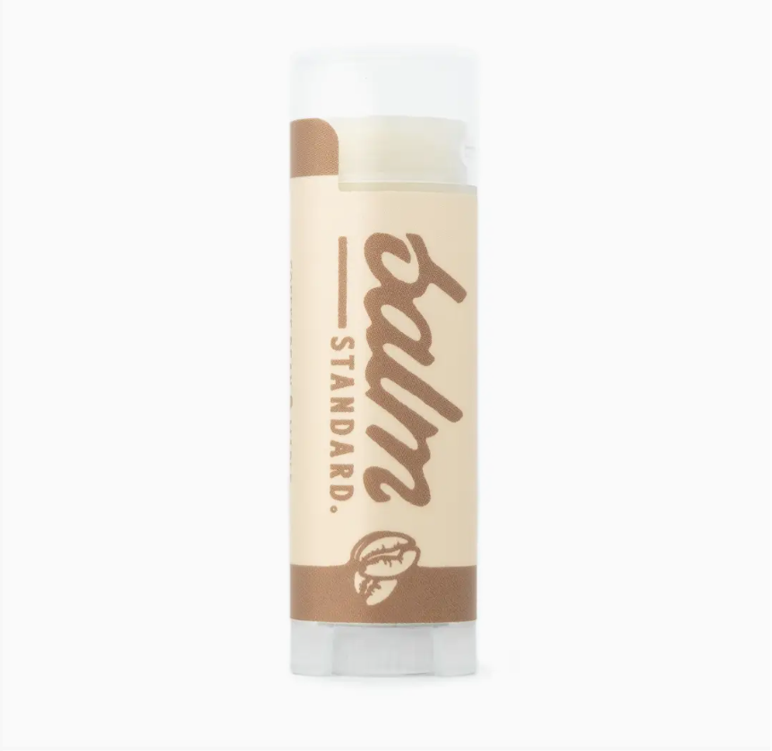 A single tube of Standard Balm lip balm on a plain white background. The tube has a beige label with brown text and graphics, a white cap, and a clear base showing the balm inside.