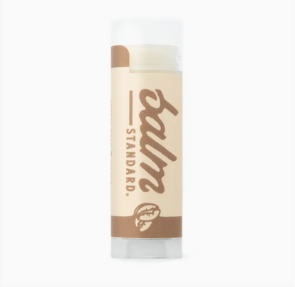 A single tube of Standard Balm lip balm on a plain white background. The tube has a beige label with brown text and graphics, a white cap, and a clear base showing the balm inside.