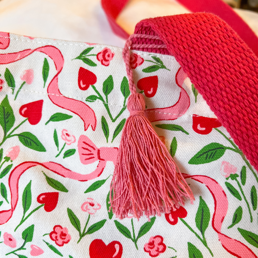 Fabric with heart and ribbon pattern and a pink tassel on a red background