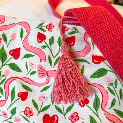 Fabric with heart and ribbon pattern and a pink tassel on a red background
