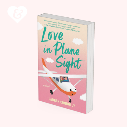 A book cover for the novel 'Love in Plane Sight' by Lauren Connolly, featuring a pink and peach gradient sky, white clouds, and an orange and white airplane. The book is shown standing upright at a slight angle on a very light pink background with a faint white heart icon in the top-left corner.