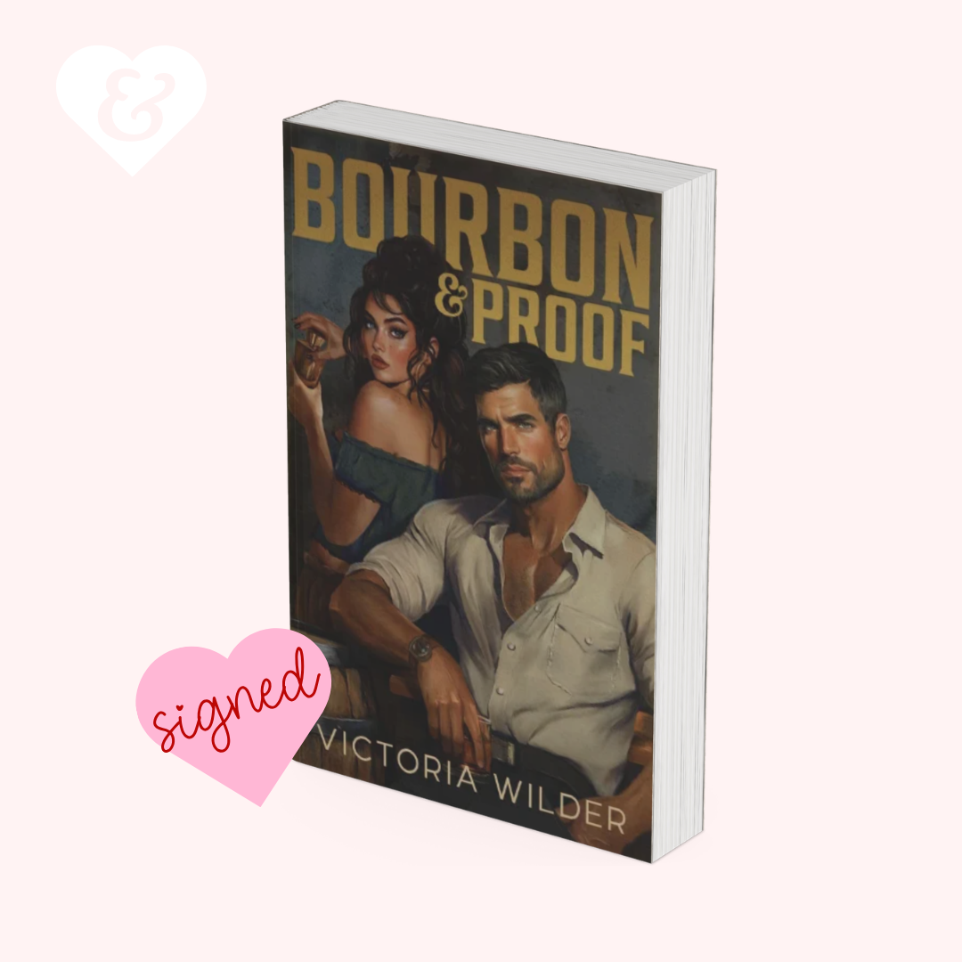 A signed copy of the book 'Bourbon & Proof' by Victoria Wilder, shown as a 3D mockup on a pale pink background with a white heart logo and a pink 'signed' heart overlay.