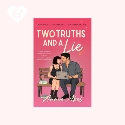 Book cover for 'Two Truths and a Lie' by Annie Abel, featuring a pink background with an illustration of a couple sitting on a bench using a laptop. The book is centered on a pale pink background with a small white heart and ampersand graphic in the top left corner.