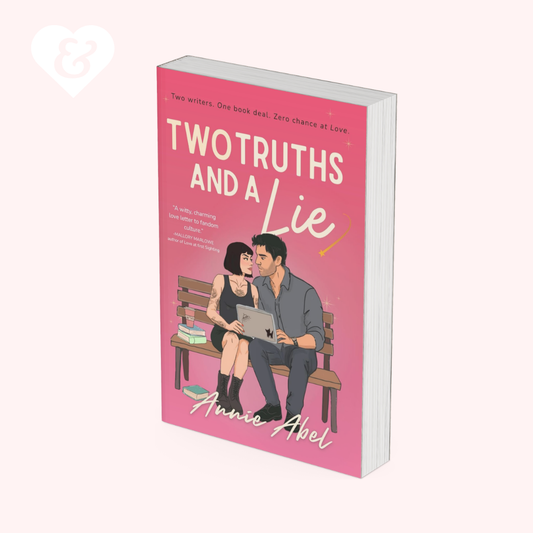 A book cover for 'Two Truths and a Lie' by Annie Abel, featuring a pink background with an illustration of a couple sitting on a bench. The book is shown at a three-quarter angle on a pale pink background with a small white heart logo in the top-left corner.