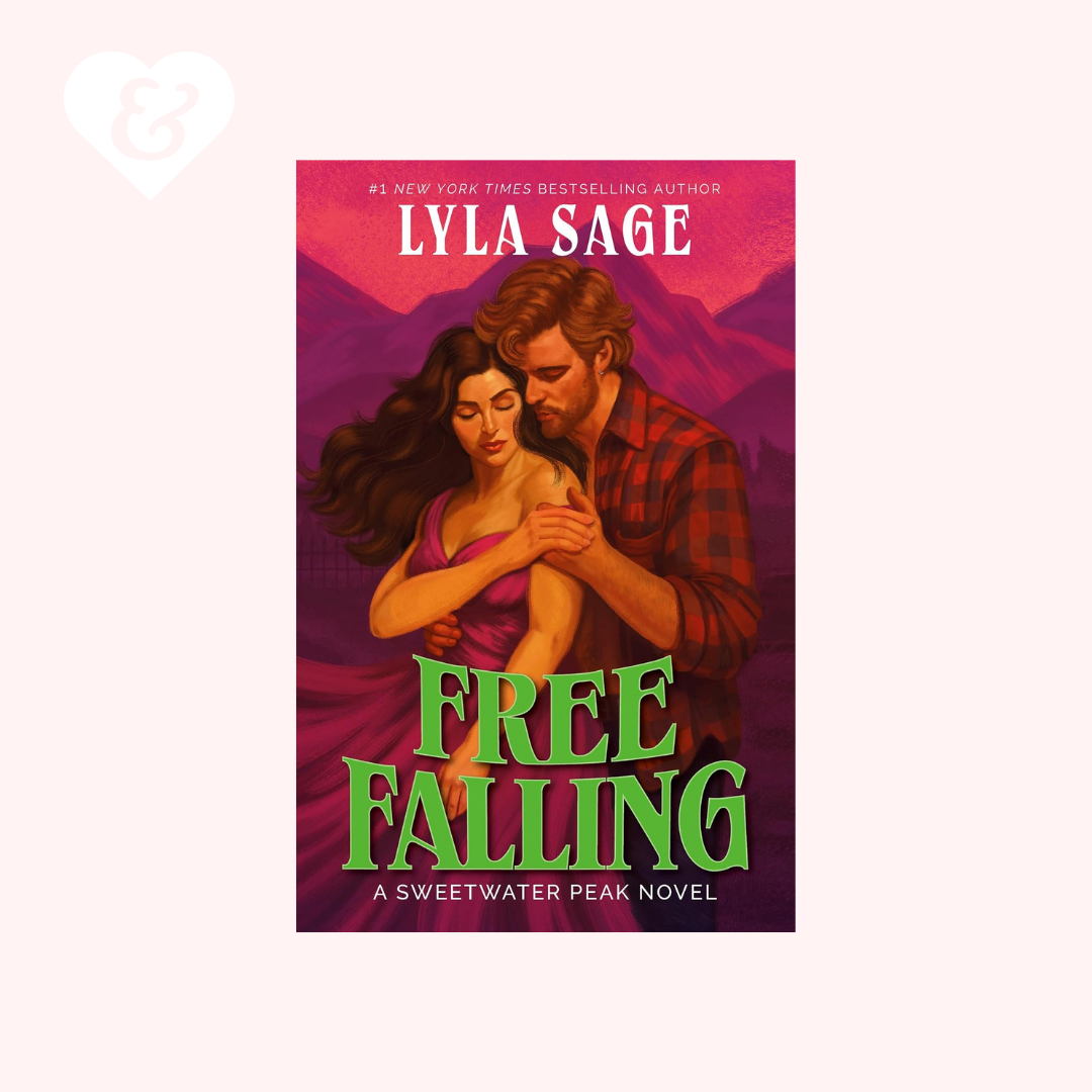 Book cover for 'Free Falling' by Lyla Sage, featuring an illustration of a man and woman embracing against a pink and purple mountain background, with the title in large green letters. The book is centered on a pale pink background with a faint white heart-and-ampersand mark in the top-left corner.