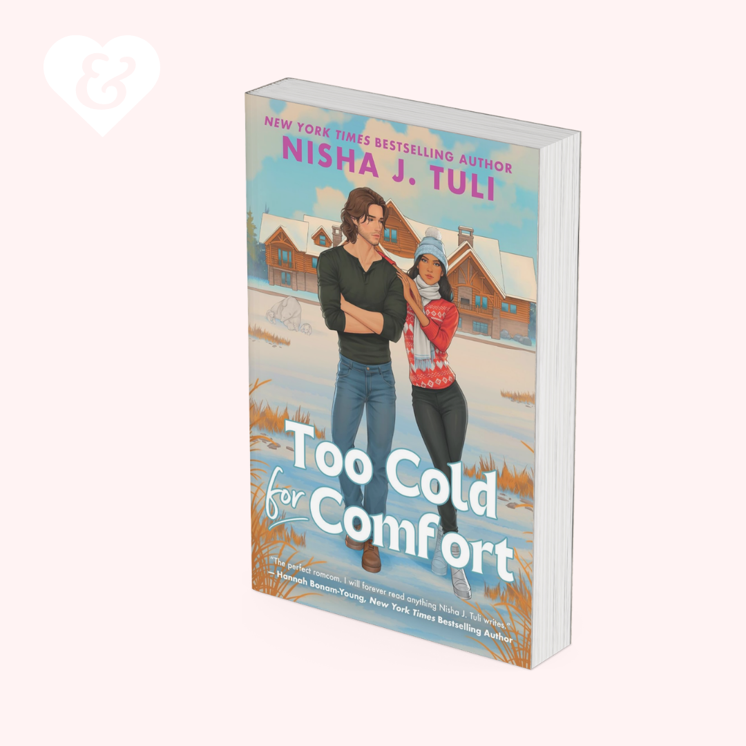A 3D mockup of the book 'Too Cold for Comfort' by Nisha J. Tuli, showing the front cover illustration of a couple in a snowy landscape and the white page edges, set against a pale pink background.