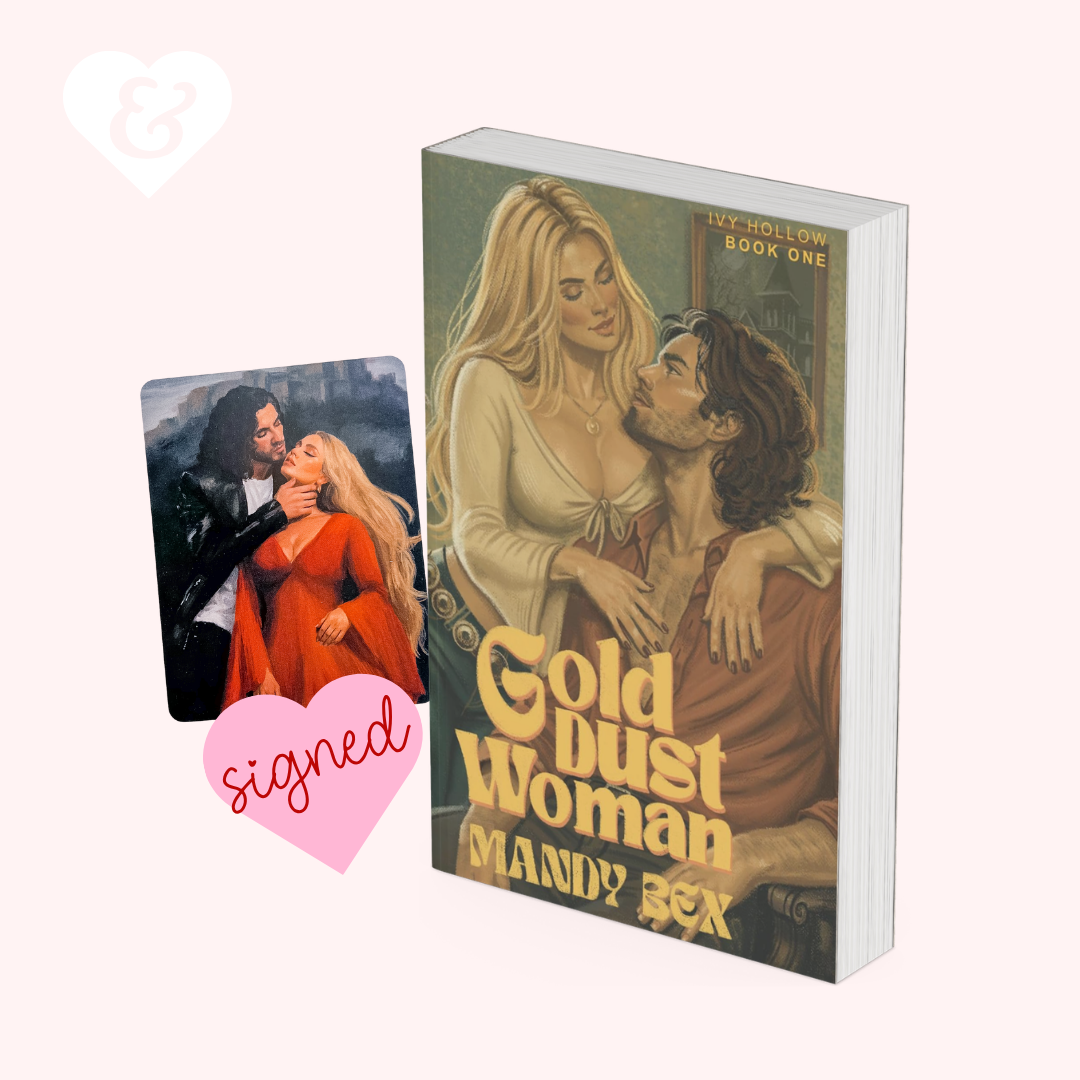 A boxed book cover for 'Gold Dust Woman' by Mandy Bex is shown on a pale pink background, alongside a small printed card featuring an illustrated couple and a pink heart-shaped 'signed' sticker graphic.