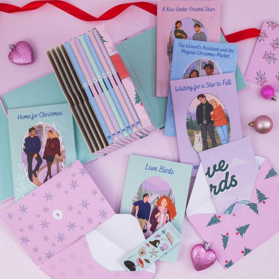 A flat-lay arrangement of Christmas-themed greeting cards and envelopes on a pink background, featuring pastel-colored envelopes, illustrated cards with couples and winter scenes, and small decorative ornaments.
