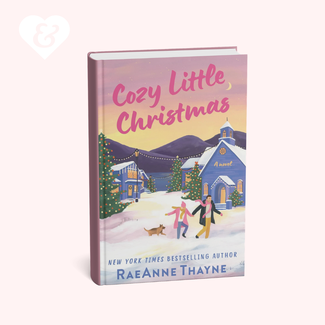 The book cover of 'Cozy Little Christmas' by RaeAnne Thayne, shown as a 3D mockup on a pale pink background. The cover features a colorful winter illustration with a blue church, snow-covered houses, and people walking in the snow.