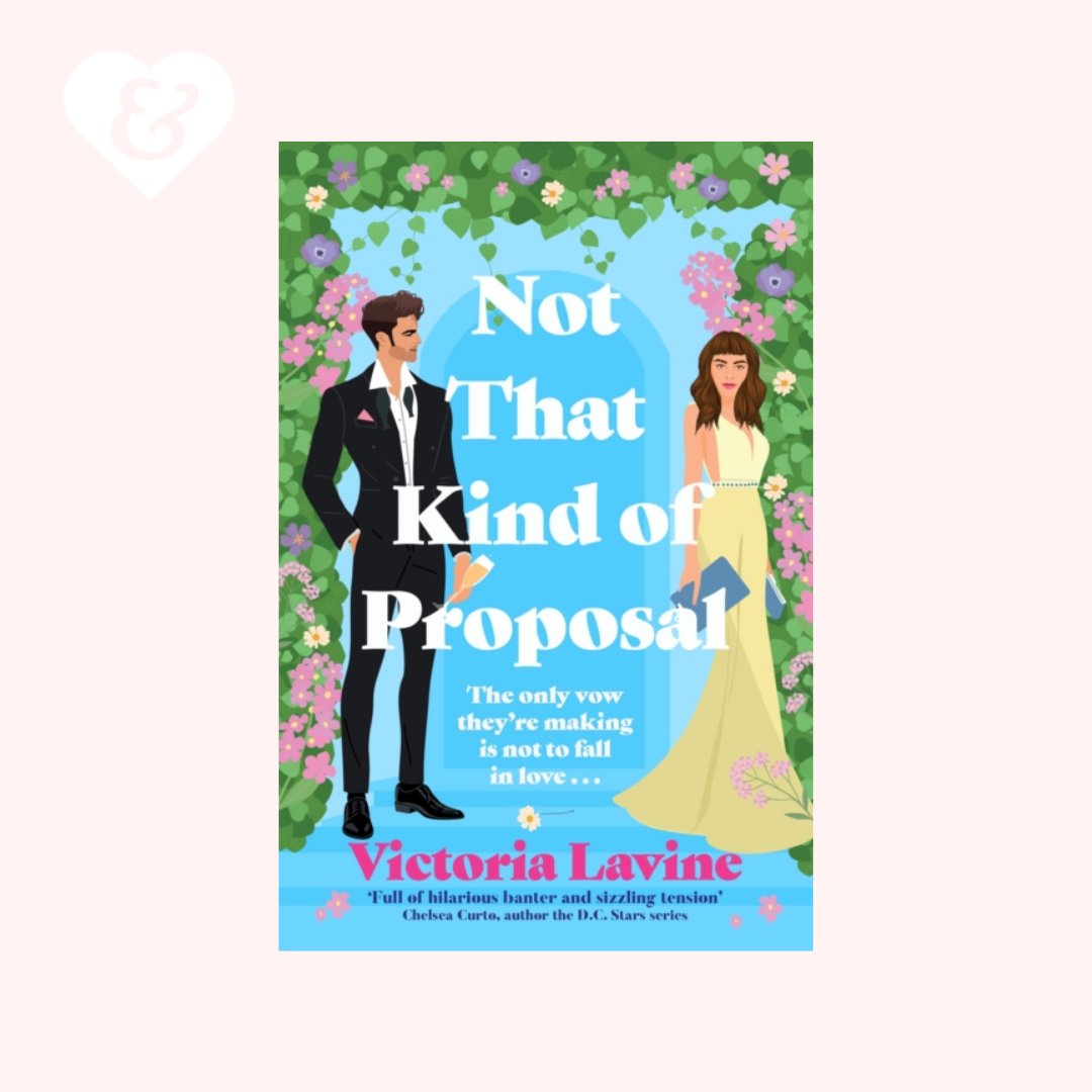 Book cover for 'Not That Kind of Proposal' by Victoria Lavine, featuring an illustrated man in a black tuxedo and a woman in a yellow wedding dress on a blue background framed by green foliage and pink flowers, shown on a pale pink backdrop.