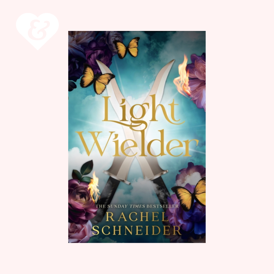 Book cover for 'Light Wielder' by Rachel Schneider, featuring two crossed silver daggers, yellow butterflies, purple flowers, and flames against a glowing blue background, centered on a pale pink backdrop with a small white heart-and-key icon in the top left.