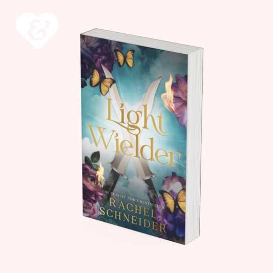 The book cover of 'Light Wielder' by Rachel Schneider, shown as a 3D mockup on a pale pink background. The cover features a teal and blue background with a large silver letter 'X' formed by two swords, surrounded by purple flowers and yellow butterflies.