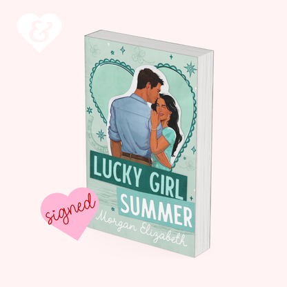 A book cover mockup for 'Lucky Girl Summer' by Morgan Elizabeth, featuring an illustration of a couple in front of a mint green heart. The book is displayed on a pale pink background with a pink 'signed' heart graphic and a white ampersand heart icon.