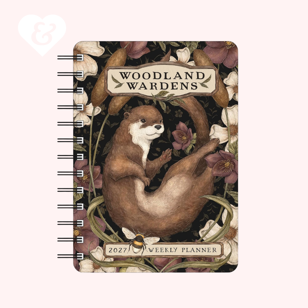 A spiral-bound 2027 weekly planner titled 'Woodland Wardens' featuring an illustration of an otter among flowers and leaves on a pale pink background.