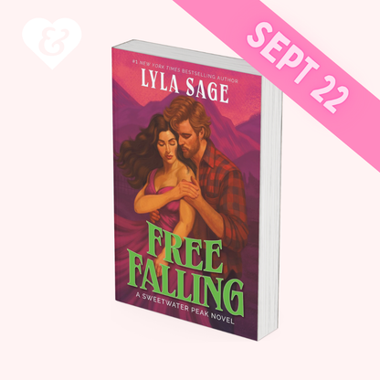 Book cover for 'Free Falling' by Lyla Sage, featuring an illustration of a man and woman embracing against a pink and purple mountain background, with the title in large green letters. The book is centered on a pale pink background with a faint white heart-and-ampersand mark in the top-left corner.