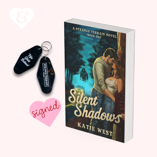 Book cover for 'Silent Shadows' by Katie West shown next to two black keychains with logo, on a pale pink background with a white heart icon and a pink 'signed' heart.