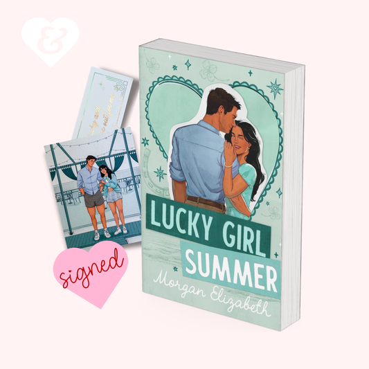 A book cover mockup for 'Lucky Girl Summer' by Morgan Elizabeth, shown standing upright with two matching printed cards or inserts beside it on a pale pink background. The cover features an illustrated couple framed by a teal heart, with the title in large teal and white lettering.
