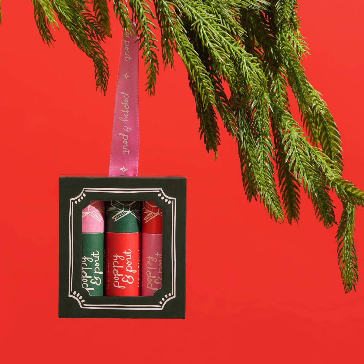 Set of lip balms in a decorative box with a pink ribbon on a red background