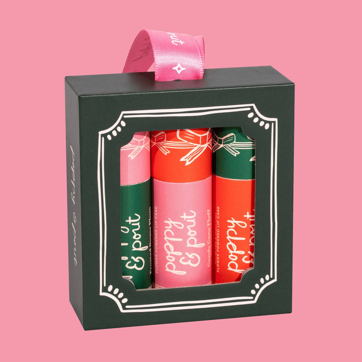 Set of three lip balms in green, pink, and red packaging with a black box on a pink background