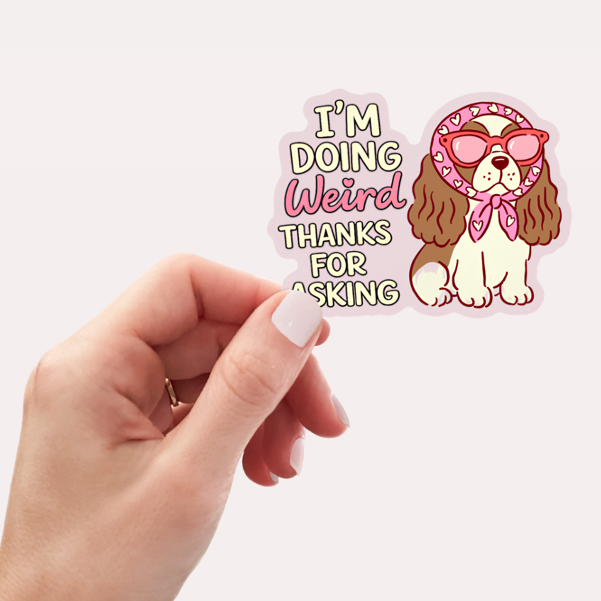 Sticker with a dog wearing sunglasses and a bandana, text 'I'm doing weird thanks for asking', held by a hand.