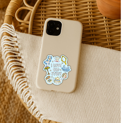 A beige phone case with a colorful retro-style sticker that reads 'LOVE OLD STUFF' with cartoon illustrations, resting on a cream fringed textile inside a wicker basket.
