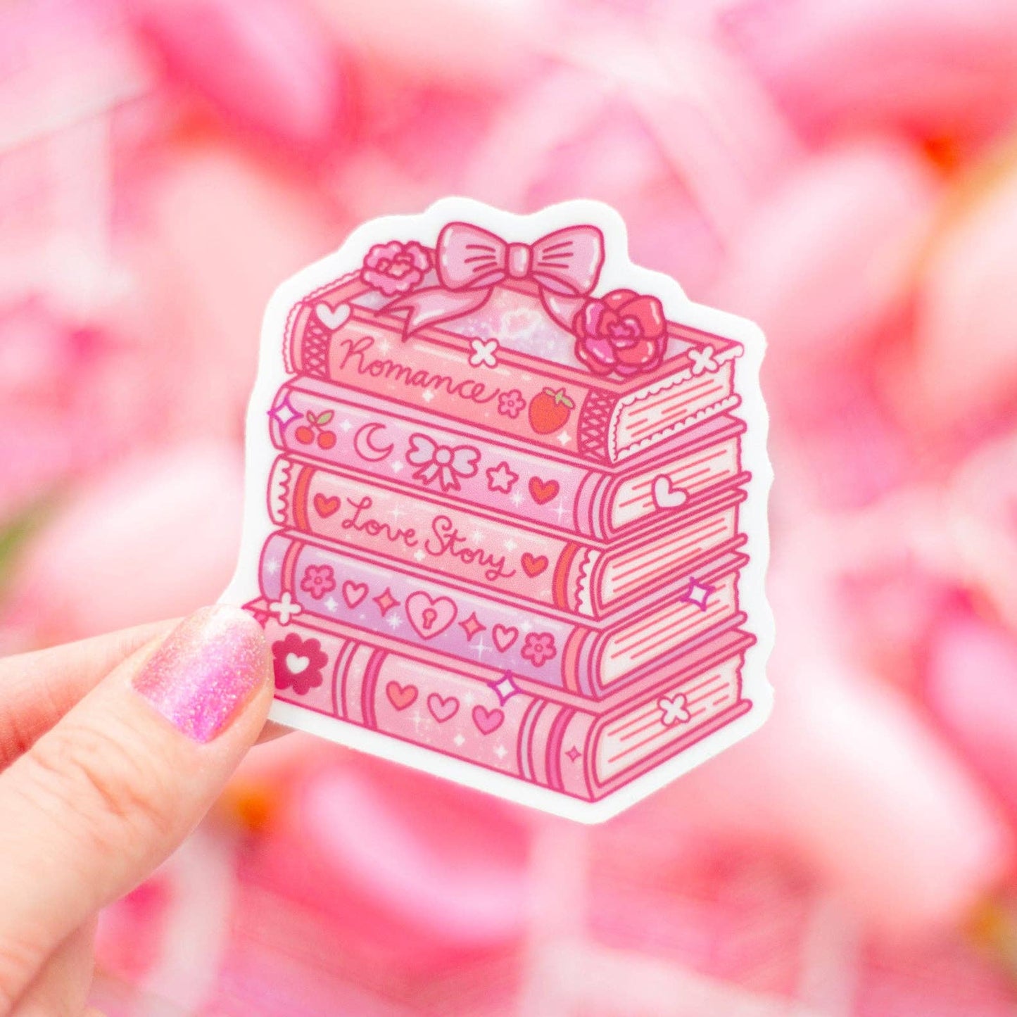 Sticker of stacked books with decorative elements held against a pink floral background